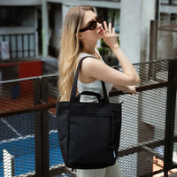 Woman holding a black tote bag outdoors