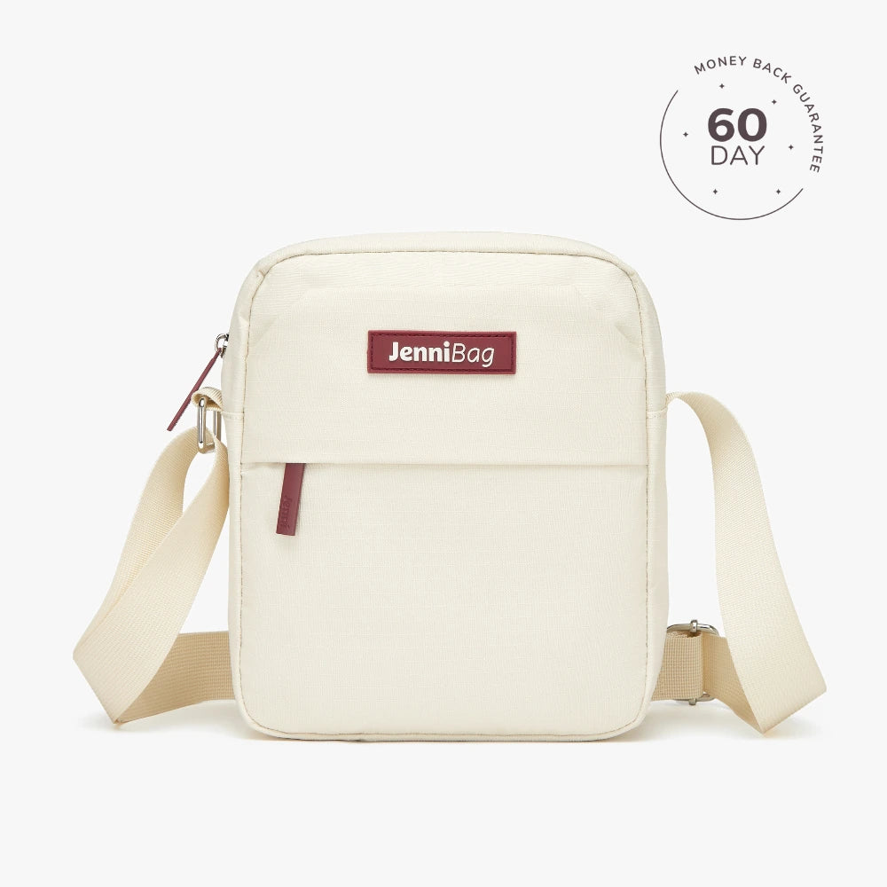 A beige Jenni crossbody bag with a zipper closure and an adjustable strap, displayed against a white background.