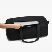 Black duffel bag with a laptop being placed inside on a white background